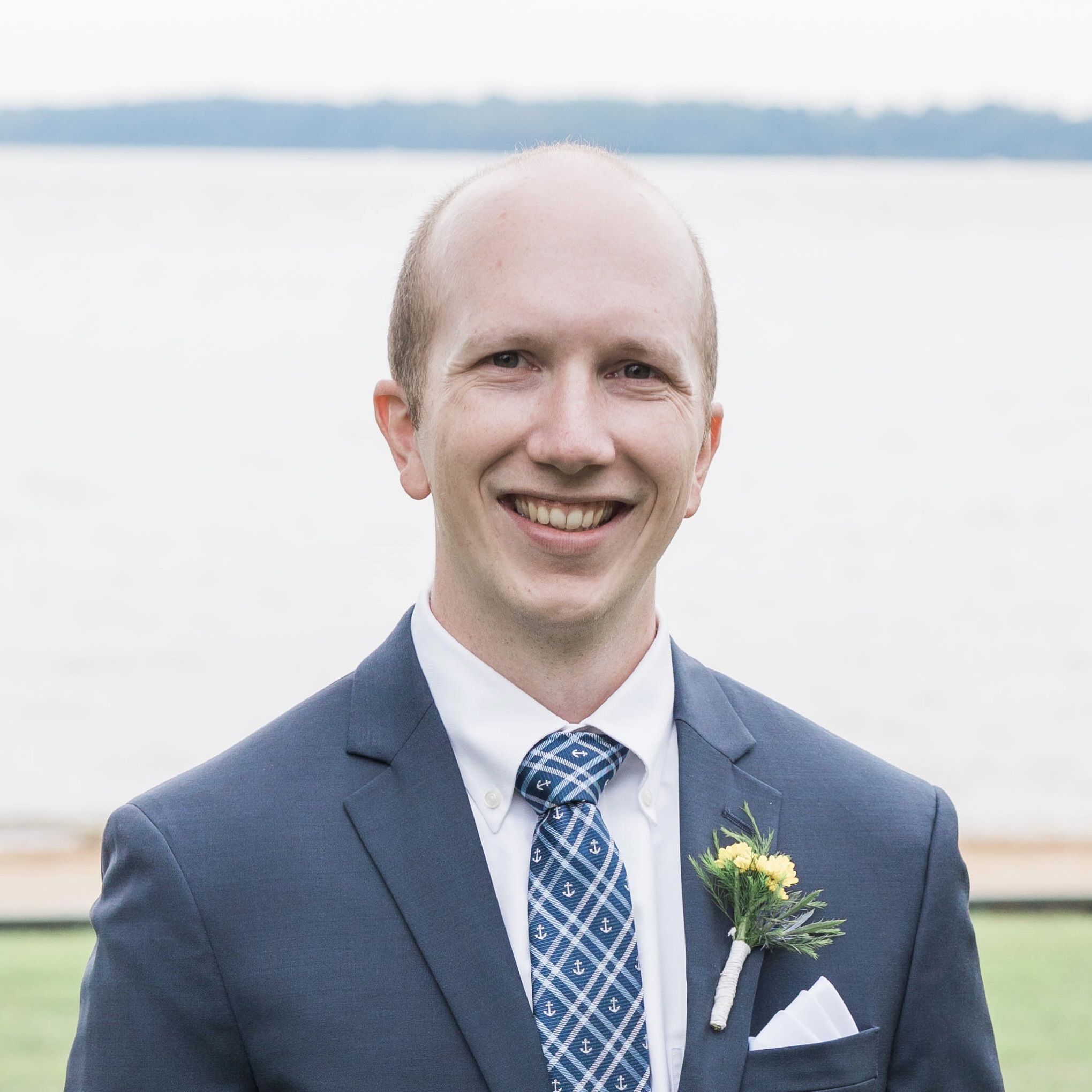 Profile photo of a man standing in a grass field next to a large body of water